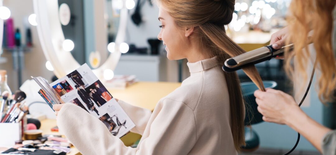 Pretty young beautiful woman client with hair stylist Photo of a concentrated young beautiful woman client reading magazine with hair stylist in saloon.